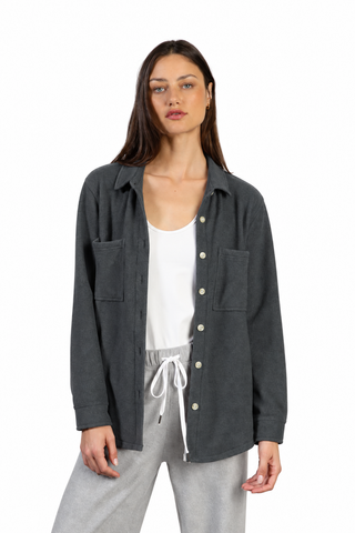 A woman modeling a dark gray button-up overshirt with two chest pockets, worn open over a white tank top and light gray sweatpants, against a plain white background.