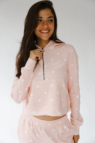 A woman wearing a light pink fleece matching set with white polka dots, featuring a cropped half-zip hoodie with 'Happy Camp3r' text and matching jogger pants, set against a plain light gray background.