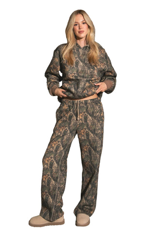 Woman wearing camouflage hunting gear standing on a wooden porch.