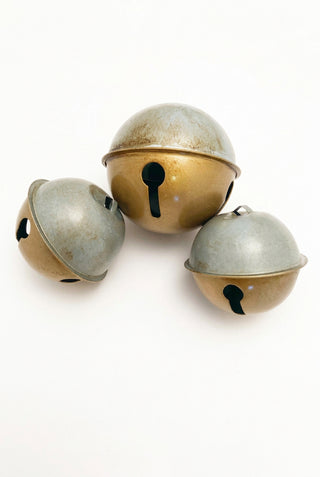 A set of three vintage-style gold Christmas bells of varying sizes arranged together.