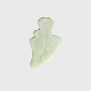 A curved, leaf-shaped, green jade gua sha tool for facial massage.